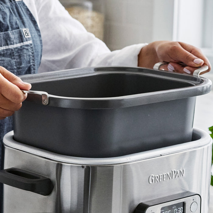 Gray pan being placed into a 7-in-1 6-quart slow cooker with in-pot browning on a kitchen counter.