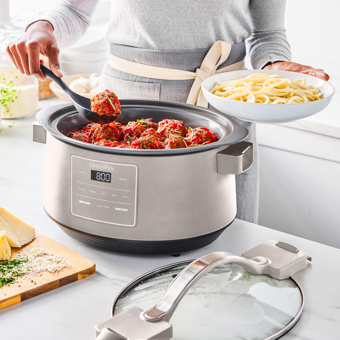 Person serving meatballs from an 8-quart slow cooker, holding a bowl of spaghetti in the other hand.