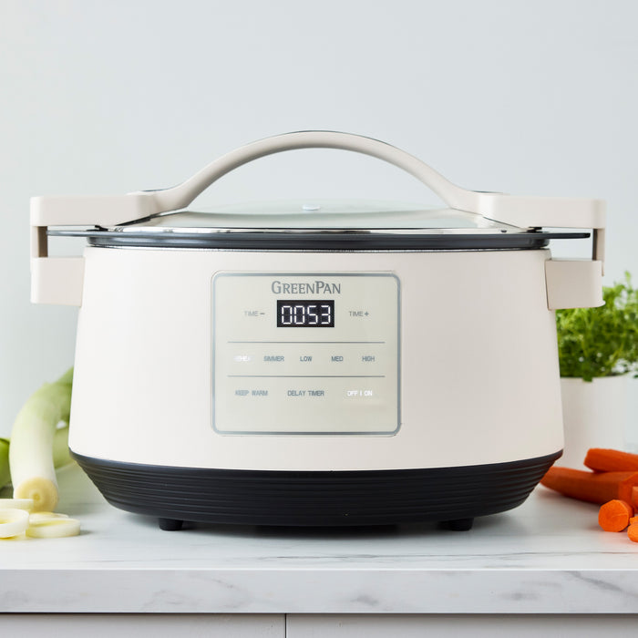 Cloud Cream 8-quart slow cooker with locking lid on a countertop next to a pile of chopped vegetables.