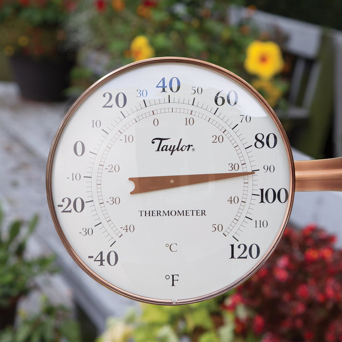 Close up of outdoor thermometer dial with Fahrenheit scale against a blurred garden background.