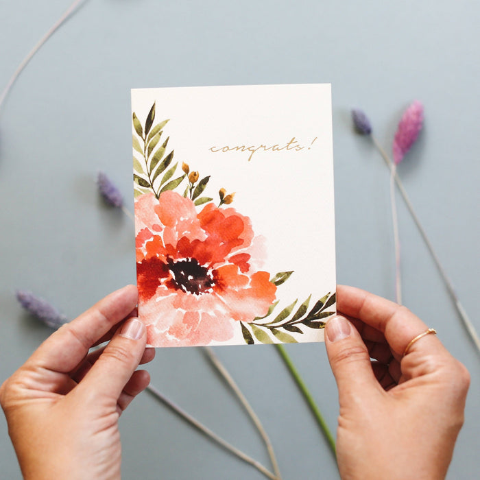 Hand holding watercolor anemone congrats greeting card with dried flowers on grey background