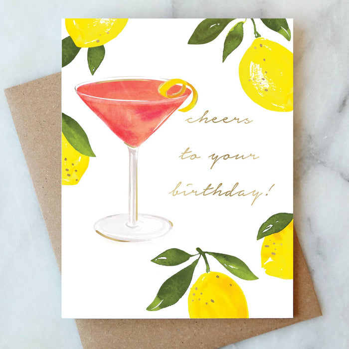 Cosmopolitan birthday greeting card with lemon illustration and kraft envelope on marble surface