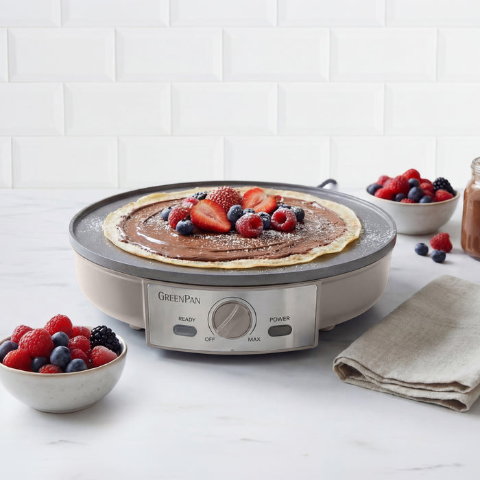 Electric crepe maker with a cooked pancake and berries on a white surface.