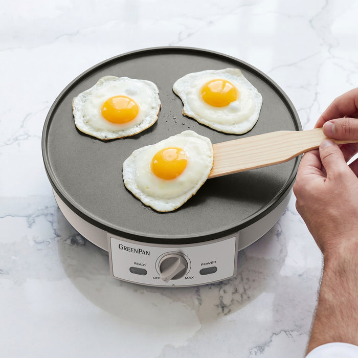 Person flipping eggs on a GreenPan electric crepe maker on a marble countertop.