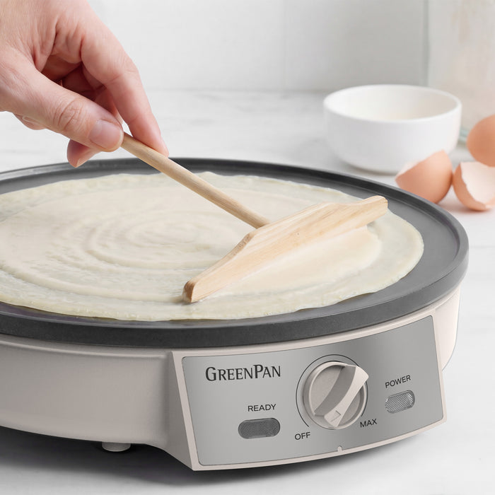 Person using a wooden spatula to spread batter on a GreenPan electric crepe maker.