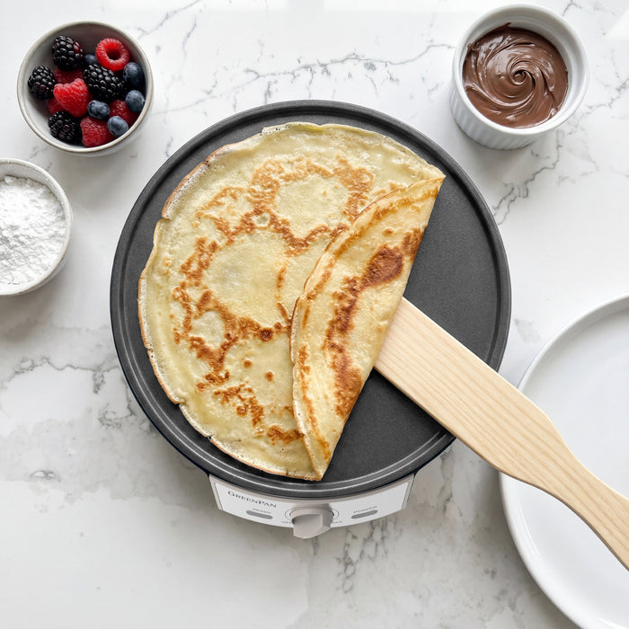 Crepe on a crepe maker with berries and Nutella nearby