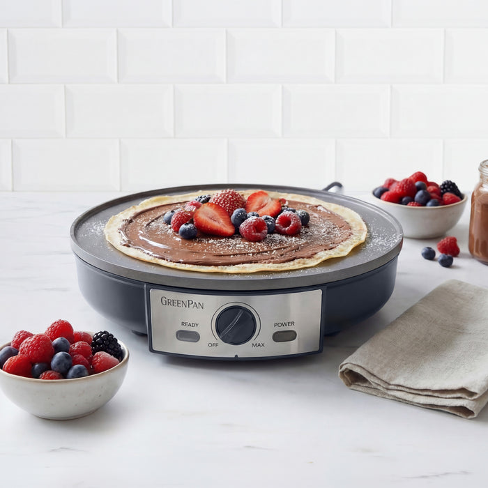 Electric crepe maker with a cooked pancake and berries on a white surface