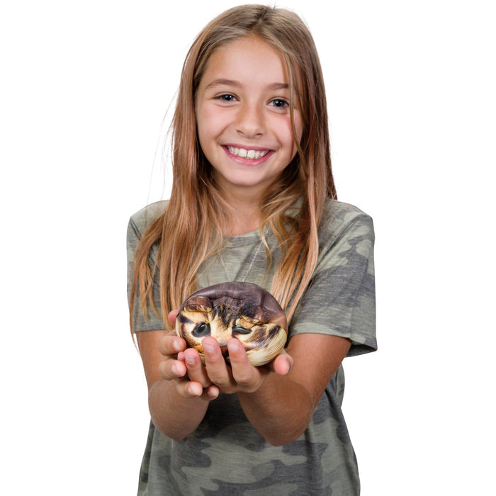 A smiling girl with long blonde hair in a camouflage shirt holds an Astroverse Catstronaut by Astroverse, curled up in her hands against a white background—an imaginative figure ready for space adventures.