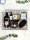 A gift box containing grooming products for men, including a beard brush, beard oil, beard and body wash, olive oil soap, chocolates, and fudge twisties.