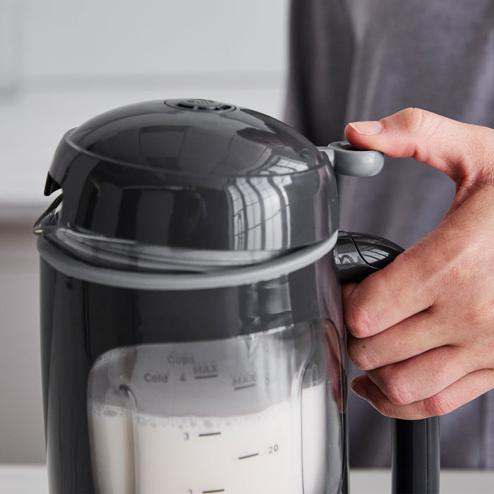 Hand pressing the lid of a graphite-colored Better Blend milk maker filled with plant-based milk.