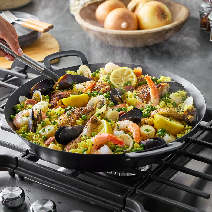 Seafood paella with shrimp and mussels in a black carbon steel paella pan on a stovetop.