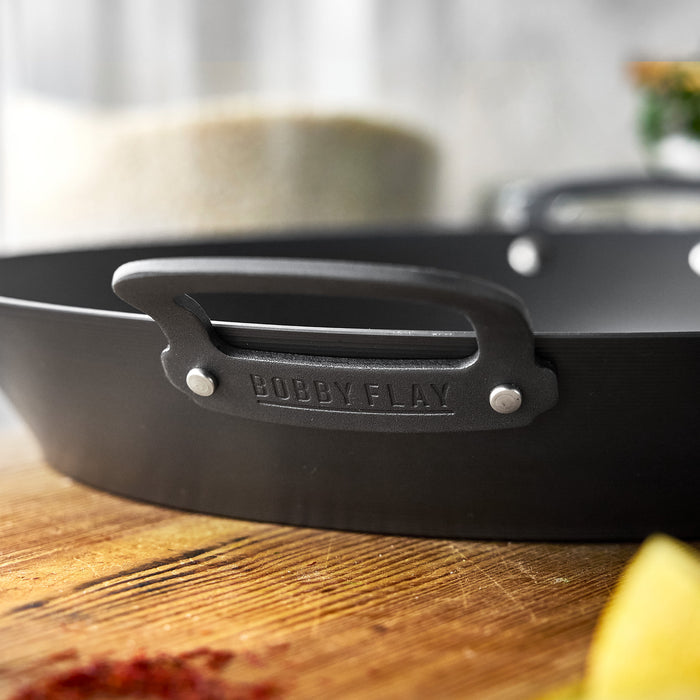 15-inch carbon steel paella pan with embossed handle on a wooden surface.