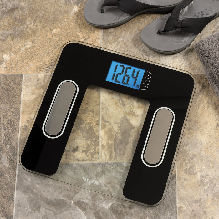 Black body composition scale on a tiled floor with gray flip flops nearby and a blue display reading 126.4 lb.