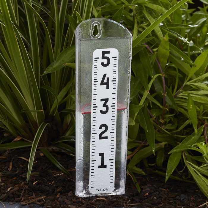 Outdoor ClearVu rain gauge mounted amid green plants with a clear tube and a large 1 to 5 scale.