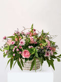 Country Basket with pastel seasonal flowers in a woven basket, featuring roses and greenery, perfect for a floral gift.