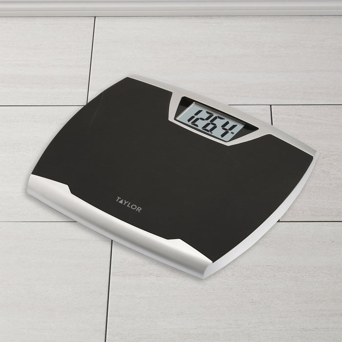Angled view of a Taylor digital bath scale on a tiled floor with a visible digital display