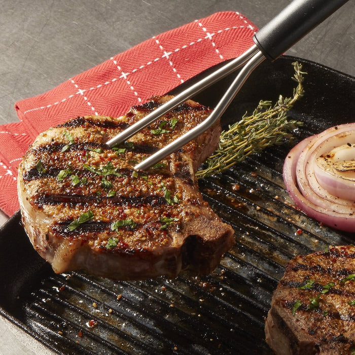 Grilled steak on a cast iron skillet checked with a two-pronged thermometer held by tongs with thyme nearby.