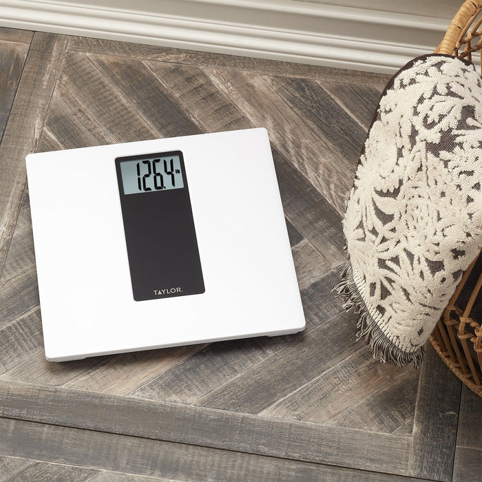 Angled view of a white Taylor digital body scale on a wooden floor with a display reading 126.4 lb.
