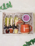 A gift set containing various skincare products and a mug with 'LOVE' written on it, presented in a wooden box lined with shredded paper.