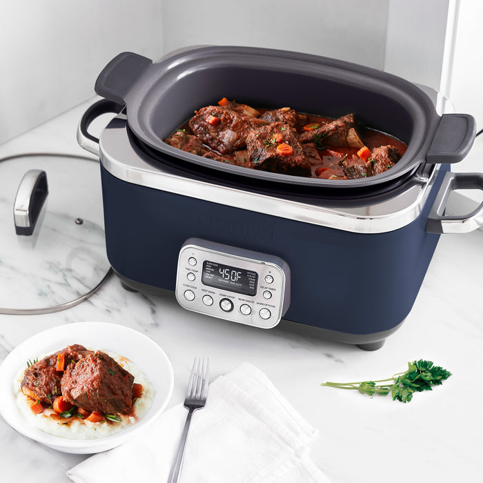 Blue slow cooker with digital display on a marble countertop, containing stewed meat and vegetables.