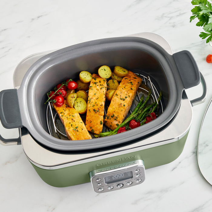 Green slow cooker with salmon and vegetables on a marble surface