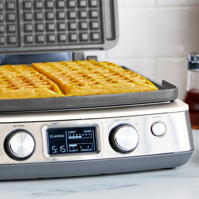 Cream ceramic 4-square waffle maker on a counter with four golden waffles inside.