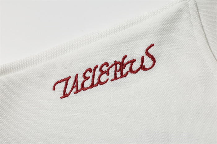 Close-up of red Taele Plus embroidery on white textured jersey fabric