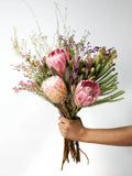Bloomable's Girl You Is Fynbos hand-held bouquet featuring soft pink king proteas, cream-pink blushing bride protea, feathery fern fronds, and delicate pink filler flowers with wispy natural elements. This artfully arranged selection of South African native flora makes an elegant gift for Mother's Day, birthdays, anniversaries, or to show appreciation with same-day delivery across South Africa.
