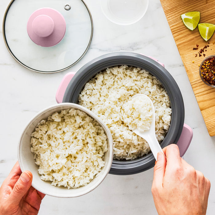 Person serving rice from a rice cooker into a bowl on a light surface.