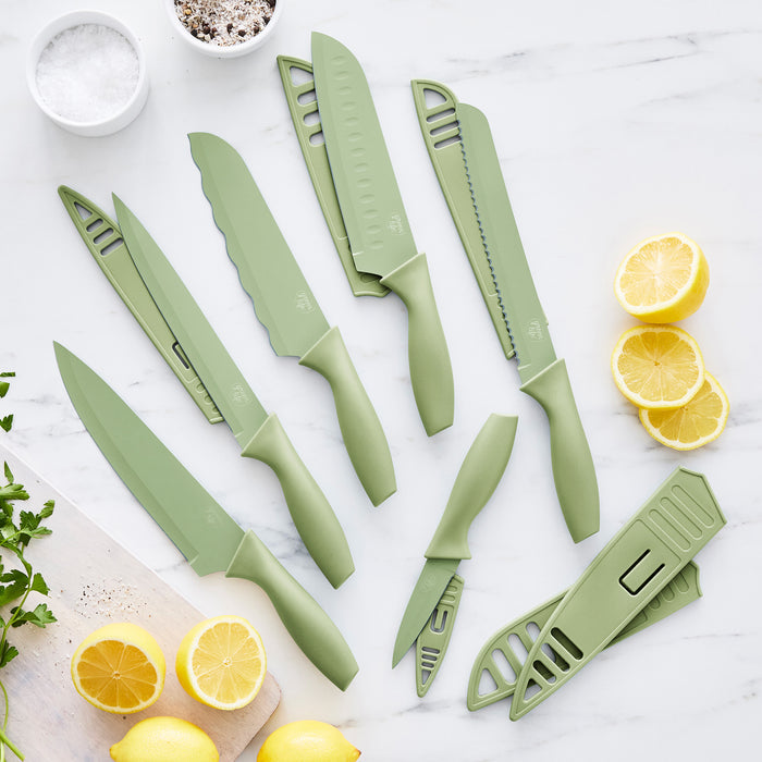 Sage green 6-piece cutlery set with blade covers on white marble, lemons, parsley, and salt nearby.