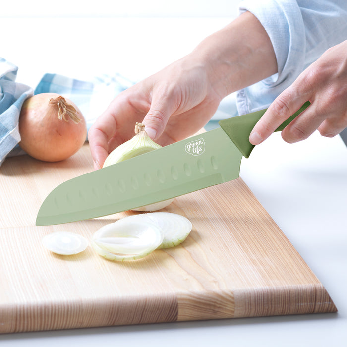 GreenLife 6-piece sage green cutlery set used to slice a white onion on a wooden cutting board.