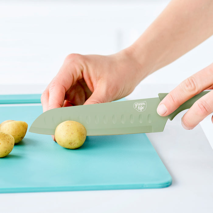 GreenLife knife slicing a small potato on a blue cutting board, two uncut potatoes next to the board.