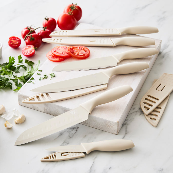 Taupe 6-piece cutlery set on a white cutting board with sliced tomatoes, herbs, and garlic around it.