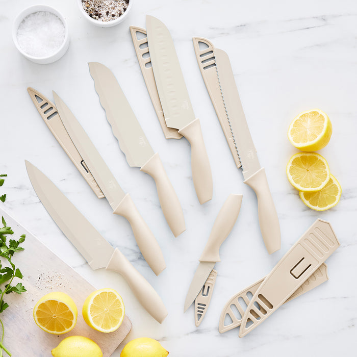 Six taupe GreenLife kitchen knives with blade covers, arranged on marble with lemon slices and a small bowl of salt.