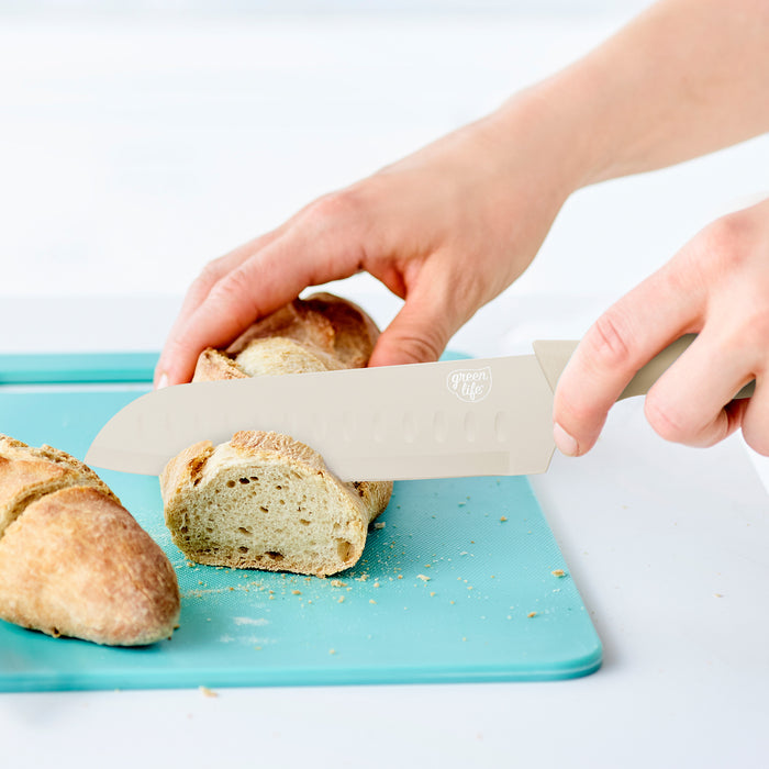 Slicing bread with a taupe GreenLife knife from the 6-piece set on a turquoise cutting board.