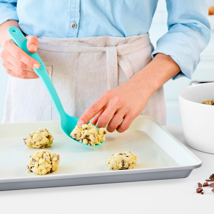 Cookie dough being spooned onto a quartz gray ceramic nonstick cookie sheet with a teal utensil.