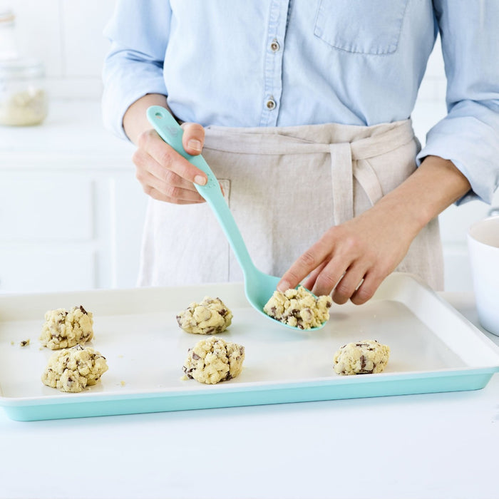 Turquoise GreenLife ceramic nonstick cookie sheet with cookie dough balls and a spatula on top.
