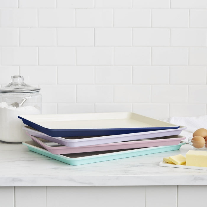 Stack of four turquoise ceramic cookie sheets on a counter with eggs, butter, and sugar nearby.