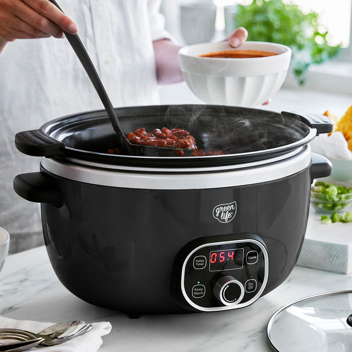 Black slow cooker with digital display on a kitchen counter, being used to serve food.