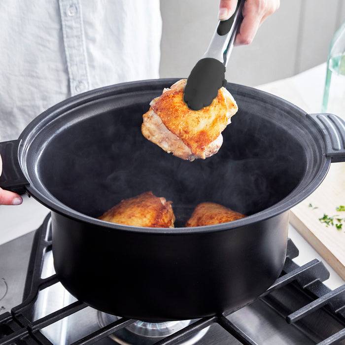 Person using tongs to place chicken into a pot on a stove