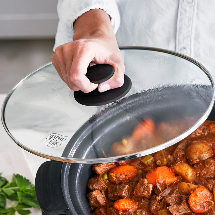 Person lifting the lid of a slow cooker filled with stew, showing carrots and beef.