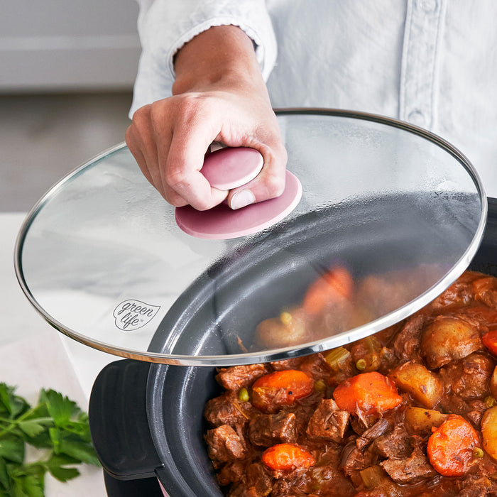 Slow cooker with lid on, filled with stew, being held by a person.