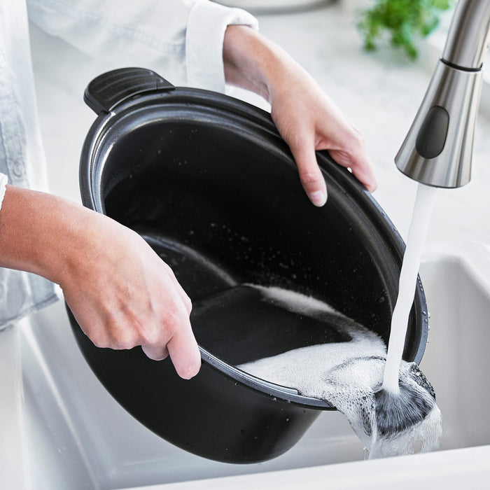 Person washing a pot under running water in a kitchen sink.
