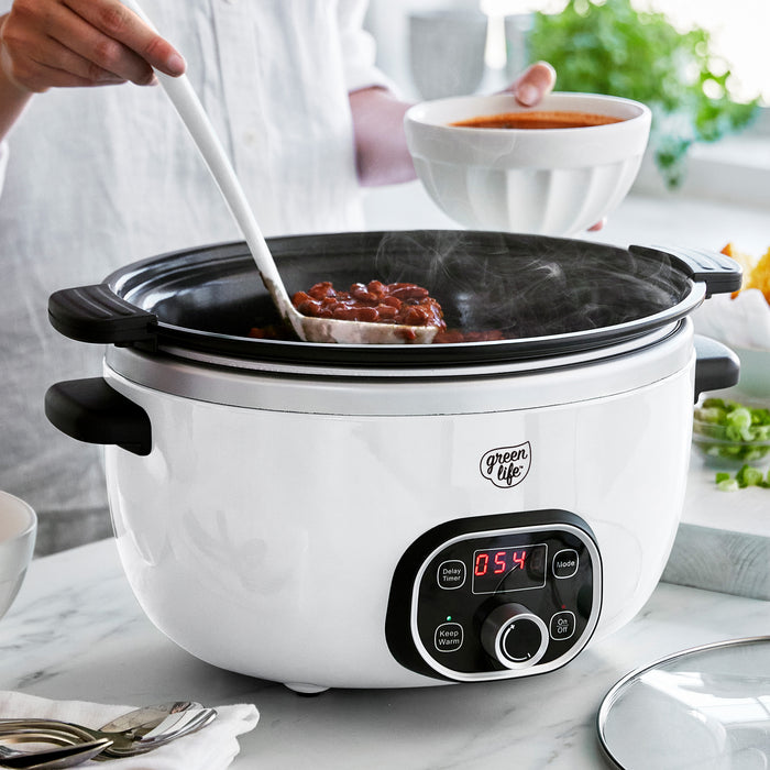 White slow cooker with digital display on a kitchen counter, being used to cook food.