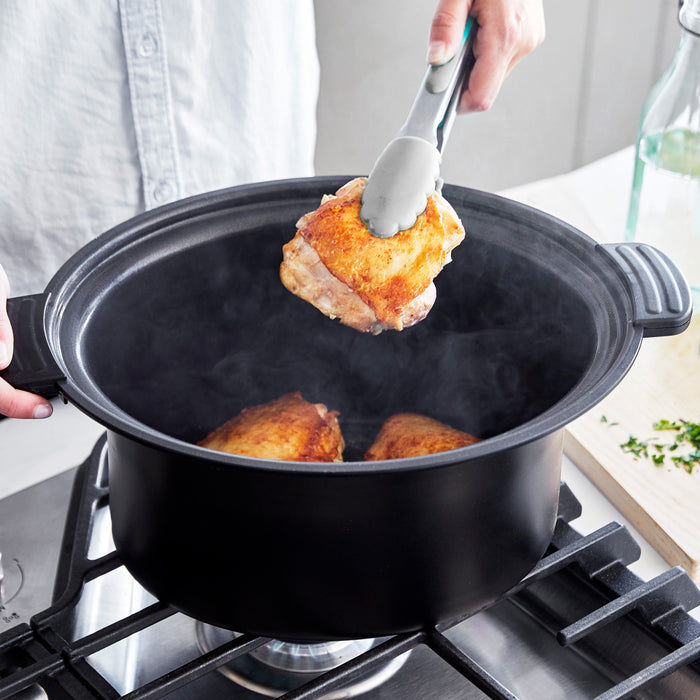 Person using tongs to remove chicken from a pot on a stove