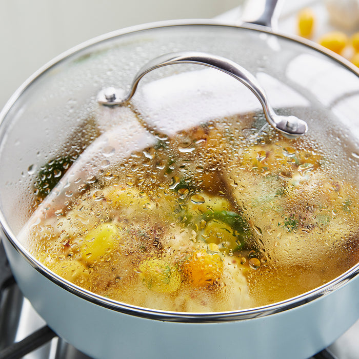 GreenPan glass lid set in 9.5 and 11 sizes covering a pot on the stove with vegetables and broth inside.
