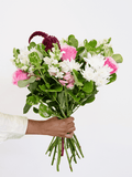 Hand holding a pink and white bouquet with greenery, featuring fresh garden blooms, ideal for gifts or special occasions.