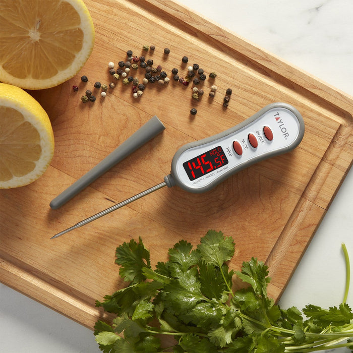 Thermometer with red digital display held over a skillet of chicken and rice with lemon halves