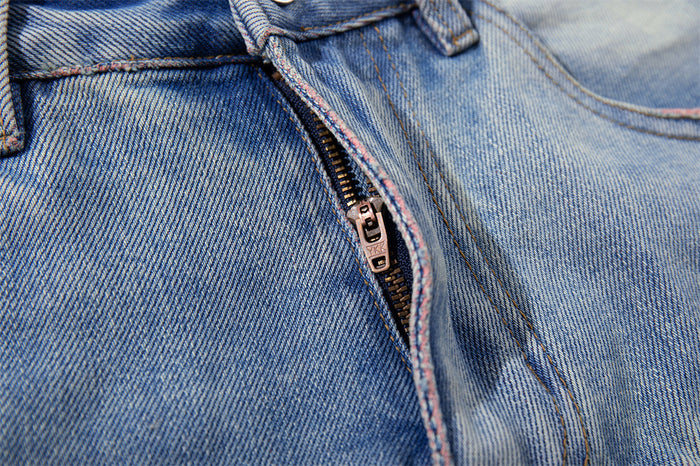 Close-up of the front zipper and fly seam on washed blue distressed denim shorts