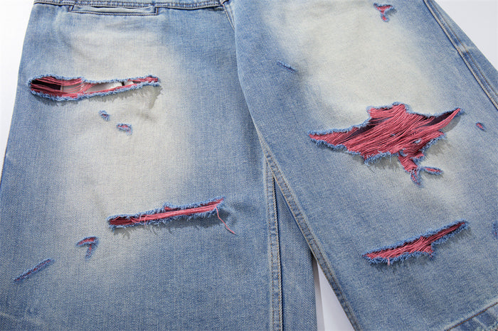 Close-up of distressed rips across washed blue denim shorts with pink threads showing through